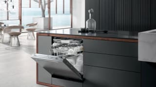 An image of a modern kitchen that includes the Miele dishwasher. Its door is open, revealing its inner racks stocked with spotless dishes.