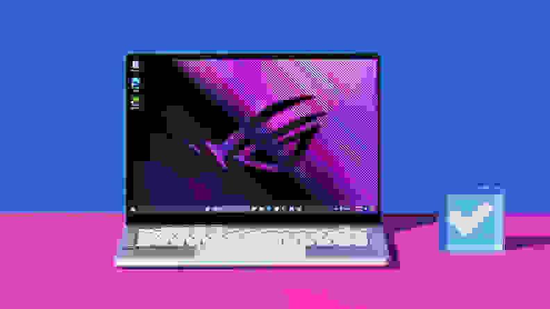 The laptop is on a pink table with a blue backdrop.