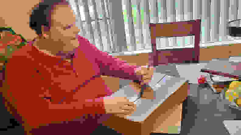 A man opening the cardboard Lego Braille Brick box with a knife.