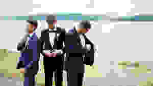 Three men standing outdoors wearing different types of suits and tuxedos.