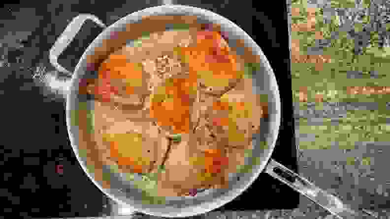 Six chicken thighs cooking in a stainless-steel pan.