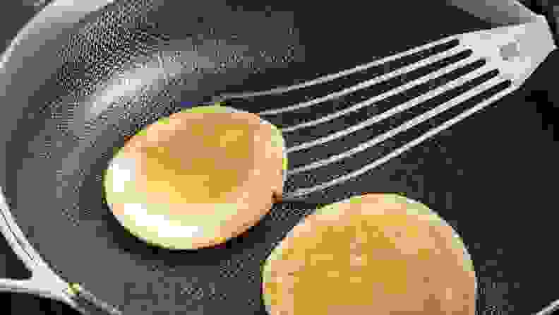 Two golden brown pancakes in the process of being flipped with spatula inside of the Always Pan Pro.