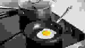 A perfect fried egg inside a nonstick pan, with a nonstick pot behind it, both sitting on a stovetop.