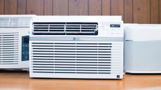Three of the best window air conditioners are displayed on a wooden countertop, all are white.