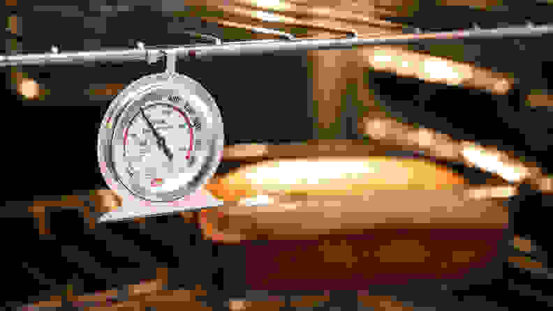 A Cooper-Atkins oven thermometer hangs inside an oven above a baking loaf cake.
