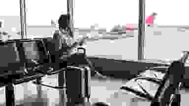 A traveler sits at a large airport window, looking at a plane outside.