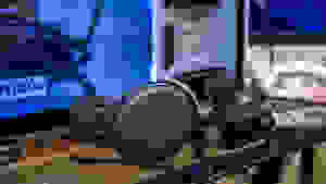 A gaming headset in black rests on a desk with gaming monitor behind it.