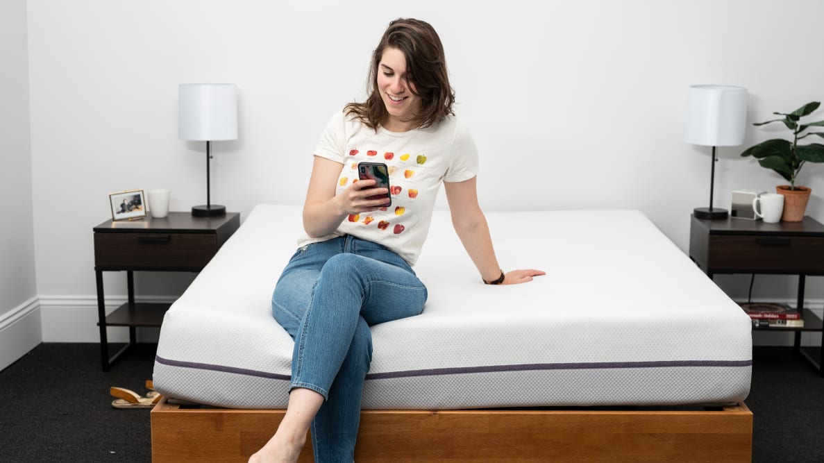 a woman sits on the foot of the Purple Mattress looking at her phone.