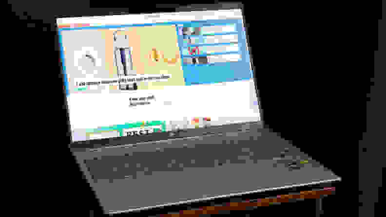 The laptop is on a black desk, the screen displaying the Reviewed website.