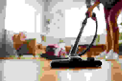 Close-up of unrecognizable woman using modern powerful hoover while vacuuming floor at home