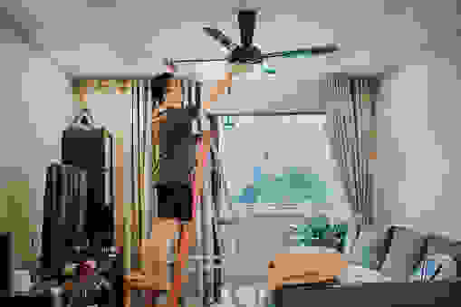 an asian chinese male cleaning ceiling fan at home