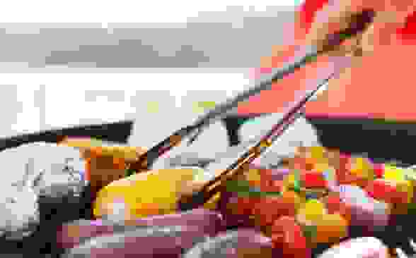 Food on a grill with corn on the cob in the center and tongs about to turn it.