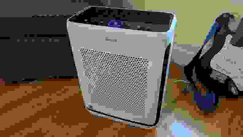 A Levoit Vital 200S air purifier in white and black sits on the floor next to a guitar.