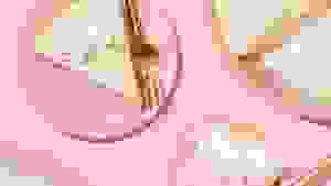A piece of regular key lime pie and a piece of strawberry key lime pie sit on two pastel pink plates, accompanied by the half-empty aluminum pie tins against a pink background.