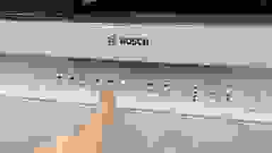 A person pointing at the Bosch 100 Series dishwasher's control buttons.