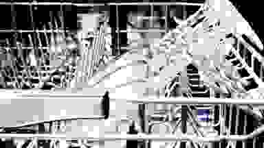 A close-up of a dishwasher's upper rack, showing wine glasses resting in stemware holders.