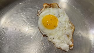 An egg cooked on a stainless-steel pan.