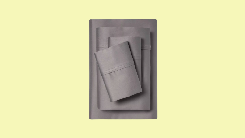 A stack of gray twin XL bed sheets sits on a pale yellow field