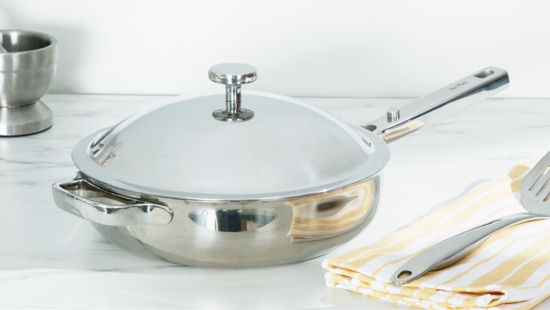 Titanium Always Pan Pro pan with lid attached next to spatula on top of a folded dishcloth.