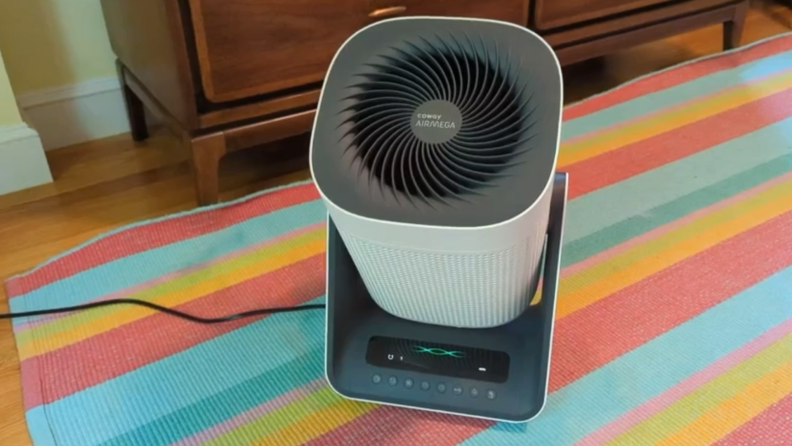 A Coway Airmega Aim air purifier sits on a floor rug.