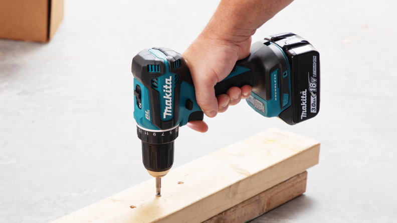 A hand holding the Makita Cordless Drill that is being used to drill into wood