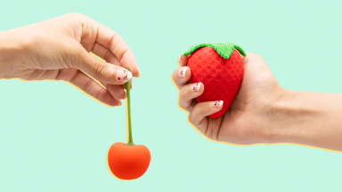 A hand holding the cherry Emojibator next to a hand holding the strawberry Emojibator