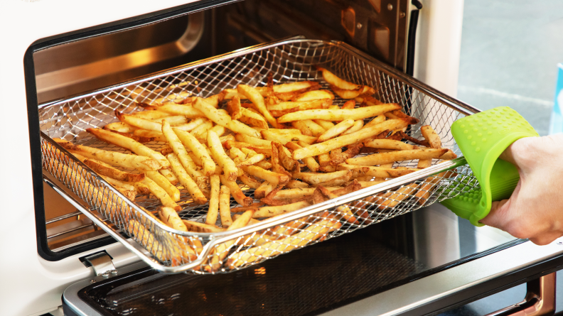 Person pulling a basket of french fries out of a countertop oven