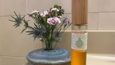 Living Libations Seabuckthorn Oil sits on a bathroom vanity in front of a floral arrangement.
