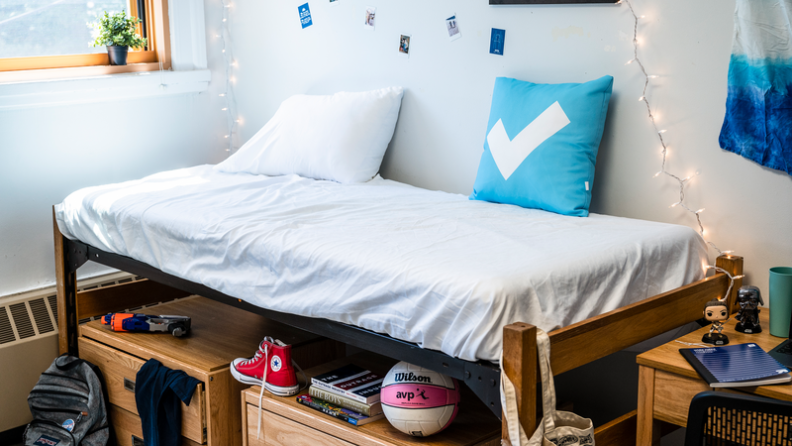 Twin XL sheets on a bed in a college dorm surrounded by shoes, clothes, decorations, and school supplies.