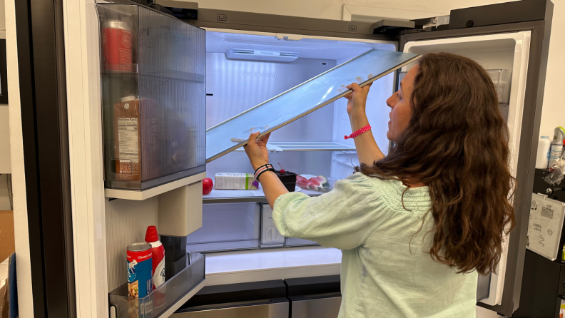 A person struggle to remove one of the interior shelves from the Samsung Bespoke RF23DB9700QL Refrigerator.