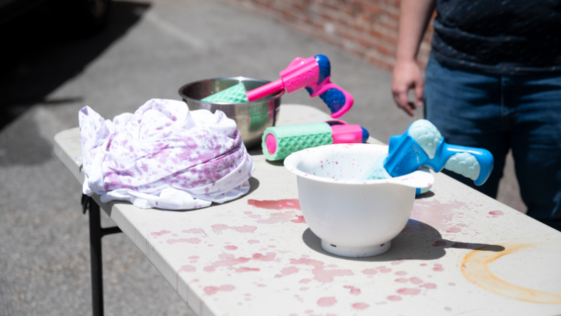 Water guns filled with wine and beer sit on bowls on a table next to a stained clump of twin XL sheets.